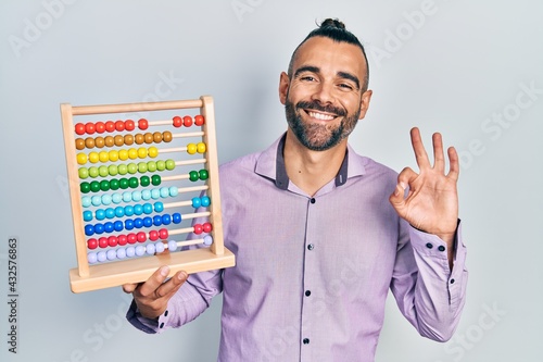 Young hispanic man holding traditional abacus doing ok sign with fingers, smiling friendly gesturing excellent symbol photo