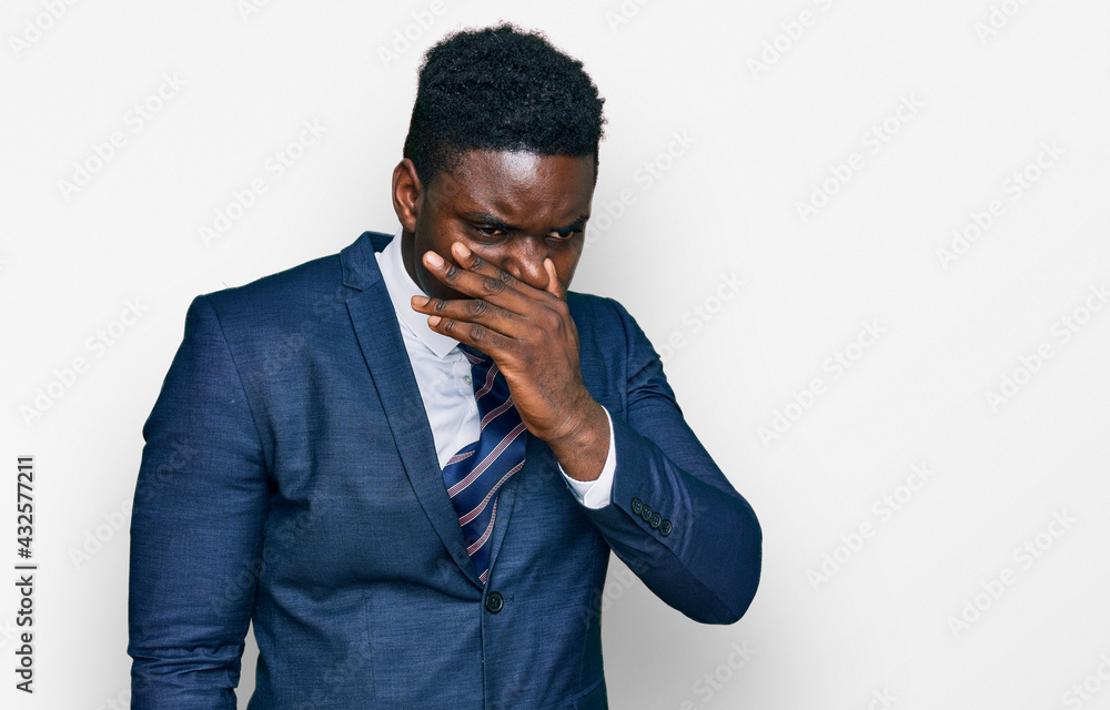 Handsome business black man wearing business suit and tie smelling something stinky and disgusting, intolerable smell, holding breath with fingers on nose. bad smell Handsome business black man wearing business suit and tie smelling something stinky and disgusting, intolerable smell, holding breath with fingers on nose. bad smell