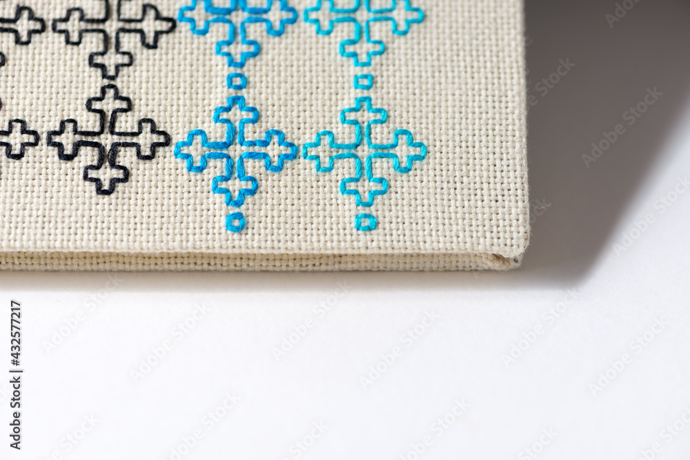 Obraz premium simple embroidery with black, blue, and cyan thread on off-white even-weave cloth, on a white background