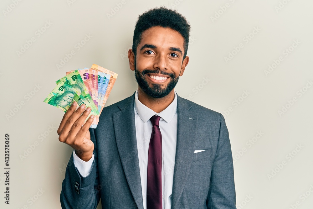 Handsome hispanic business man with beard holding south african rand banknotes looking positive and happy standing and smiling with a confident smile showing teeth Handsome hispanic business man with beard holding south african rand banknotes looking positive and happy standing and smiling with a confident smile showing teeth