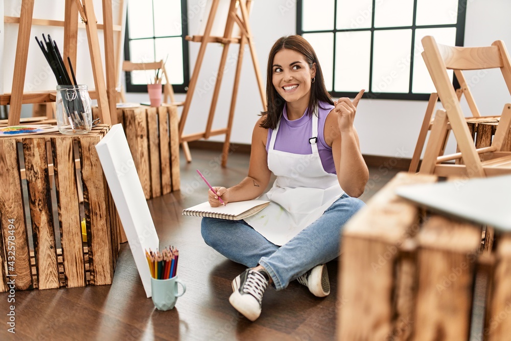 Young beautiful hispanic woman at art studio smiling happy pointing with hand and finger to the side Young beautiful hispanic woman at art studio smiling happy pointing with hand and finger to the side