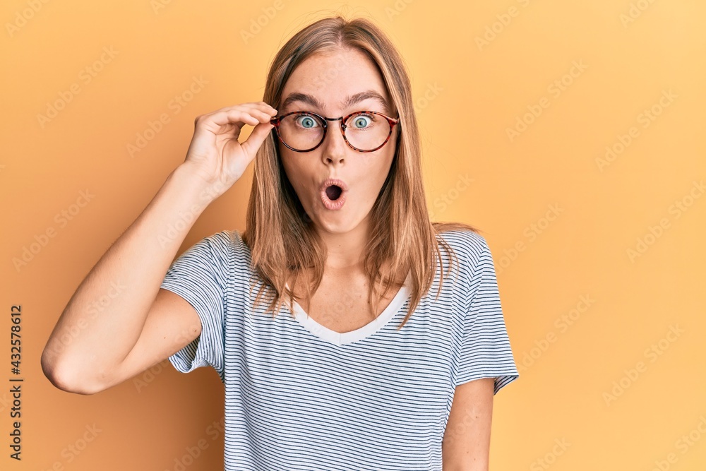 Beautiful blonde woman wearing casual clothes and holding glasses scared and amazed with open mouth for surprise, disbelief face