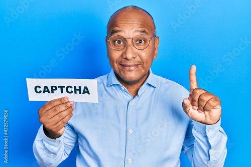 Middle age latin man holding captcha message paper smiling with an idea or question pointing finger with happy face, number one photo