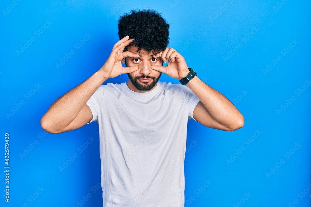 Young arab man with beard wearing casual white t shirt trying to open eyes with fingers, sleepy and tired for morning fatigue Young arab man with beard wearing casual white t shirt trying to open eyes with fingers, sleepy and tired for morning fatigue