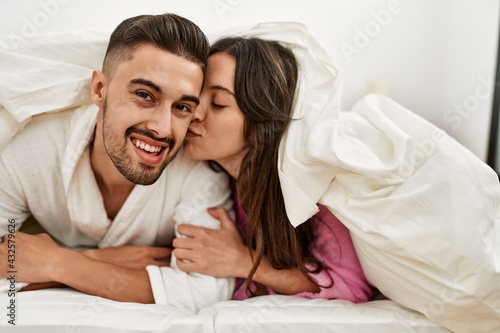 Young hispanic couple lying in bed kissing at home.