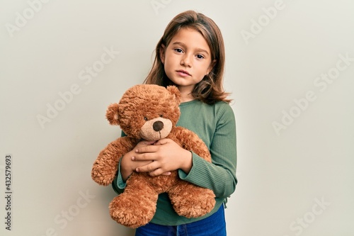 Little beautiful girl hugging teddy bear relaxed with serious expression on face. simple and natural looking at the camera.
