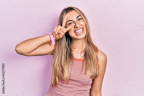 Beautiful hispanic woman wearing casual summer t shirt doing peace symbol with fingers over face, smiling cheerful showing victory