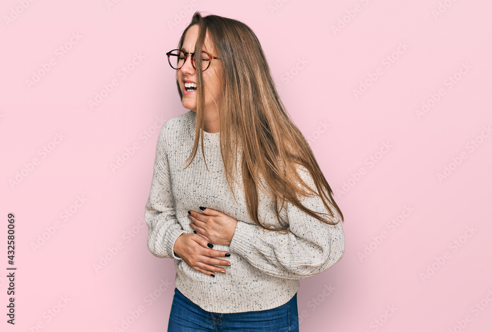 Young blonde woman wearing casual sweater and glasses with hand on stomach because nausea, painful disease feeling unwell. ache concept. Young blonde woman wearing casual sweater and glasses with hand on stomach because nausea, painful disease feeling unwell. ache concept.