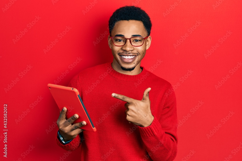 Young african american man using touchpad device smiling happy pointing with hand and finger Young african american man using touchpad device smiling happy pointing with hand and finger