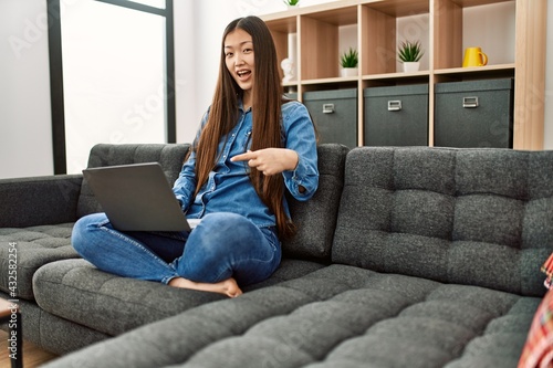 Young chinese girl wearing casual clothes working using laptop at home smiling happy pointing with hand and finger
