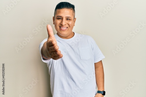 Young latin man wearing casual white t shirt smiling friendly offering handshake as greeting and welcoming. successful business.