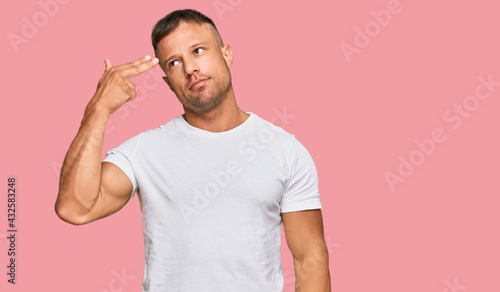 Foto Handsome muscle man wearing casual white tshirt shooting and killing oneself pointing hand and fingers to head like gun, suicide gesture