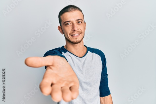 Hispanic young man wearing casual clothes smiling friendly offering handshake as greeting and welcoming. successful business.