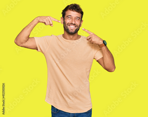Handsome young man with beard wearing casual tshirt smiling cheerful showing and pointing with fingers teeth and mouth. dental health concept. © Krakenimages.com