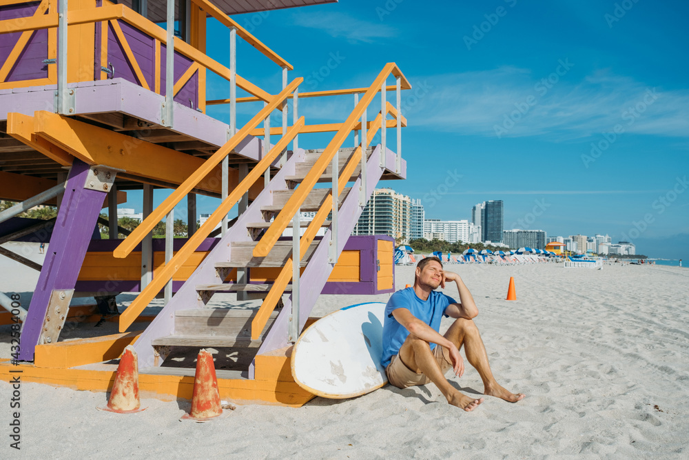 Guy walking along the empty sandy Miami beach. Happy handsome man tourist in casual clothes sitting on sandy beach. Travel and tourism concept.