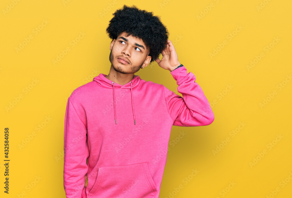 Young african american man with afro hair wearing casual pink sweatshirt confuse and wondering about question. uncertain with doubt, thinking with hand on head. pensive concept. Young african american man with afro hair wearing casual pink sweatshirt confuse and wondering about question. uncertain with doubt, thinking with hand on head. pensive concept.