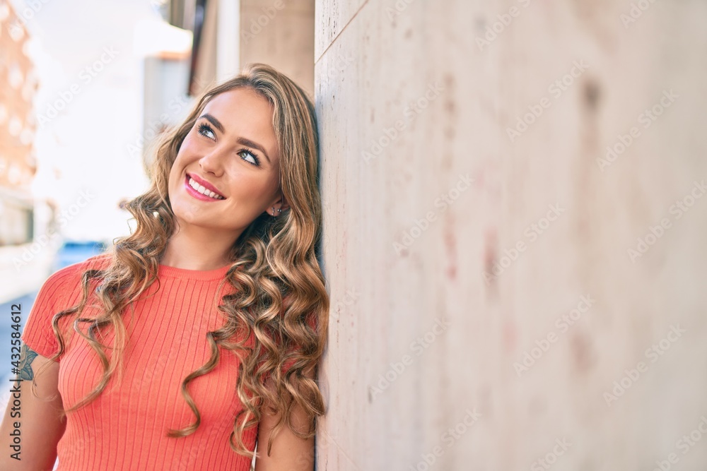 Fototapeta premium Young blonde girl smiling happy leaning on the wall at the city.