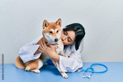 Veterinarian woman wearing uniform at the clinic, hugging dog with love