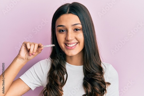 Young hispanic woman holding invisible aligner orthodontic looking positive and happy standing and smiling with a confident smile showing teeth
