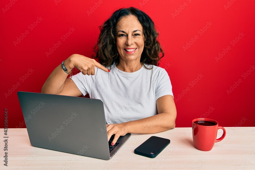 Fototapeta premium Beautiful middle age woman working at the office using computer laptop pointing finger to one self smiling happy and proud