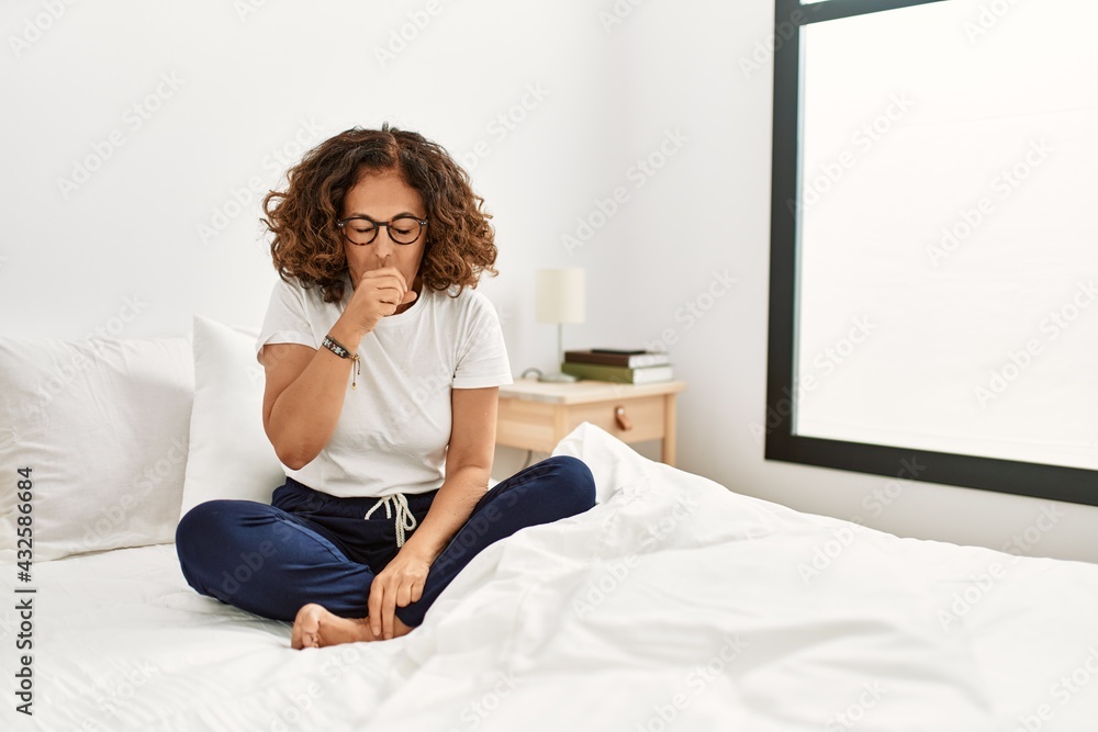 Middle age hispanic woman sitting on the bed at home feeling unwell and coughing as symptom for cold or bronchitis. health care concept. Middle age hispanic woman sitting on the bed at home feeling unwell and coughing as symptom for cold or bronchitis. health care concept.