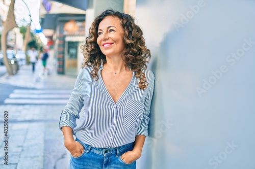 Obraz na plátně Middle age hispanic woman smiling happy leaning on the wall at the city