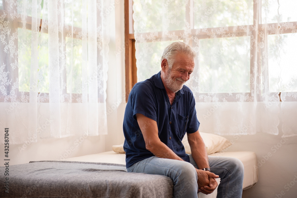 Depressed Caucasian senior man sit on the bed and looking down in bedroom. Loneliness elderly male living alone at home with sadness worry about health problem. Retirement mental health care concept
