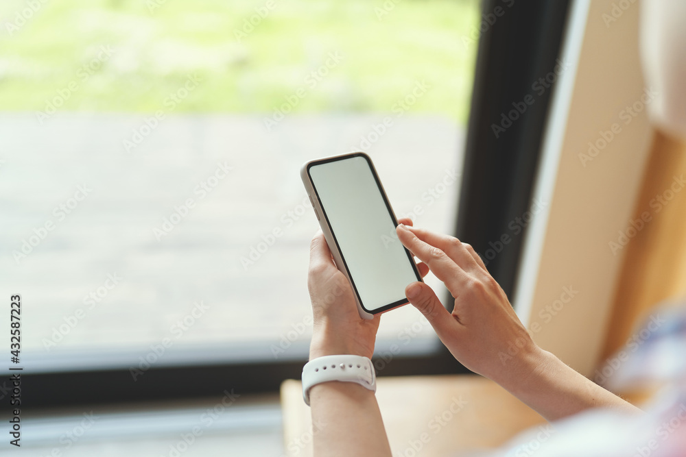 Side view of mockup image of a woman holding smartphone near the window