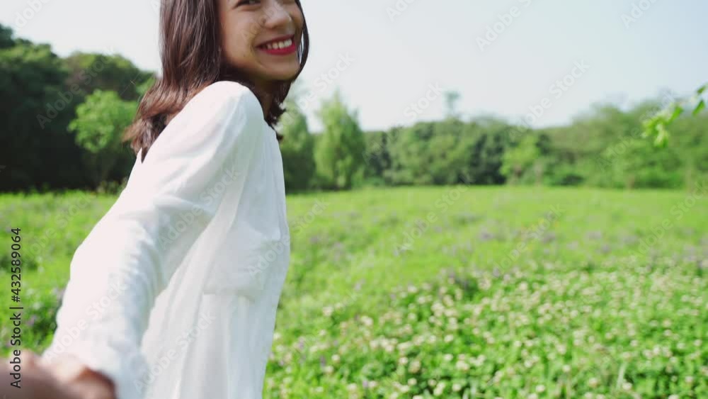 4k slow motion POV Young beautiful Asian girlfriend holding hands happily walking on the grass full of flowers looking back at camera smile
