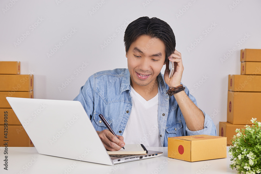 Online Merchant or Casual Businessman in Online Store Using Smartphone to Talk with Customer and Writing Product Detail in Notebook Online Merchant or Casual Businessman in Online Store Using Smartphone to Talk with Customer and Writing Product Detail in Notebook