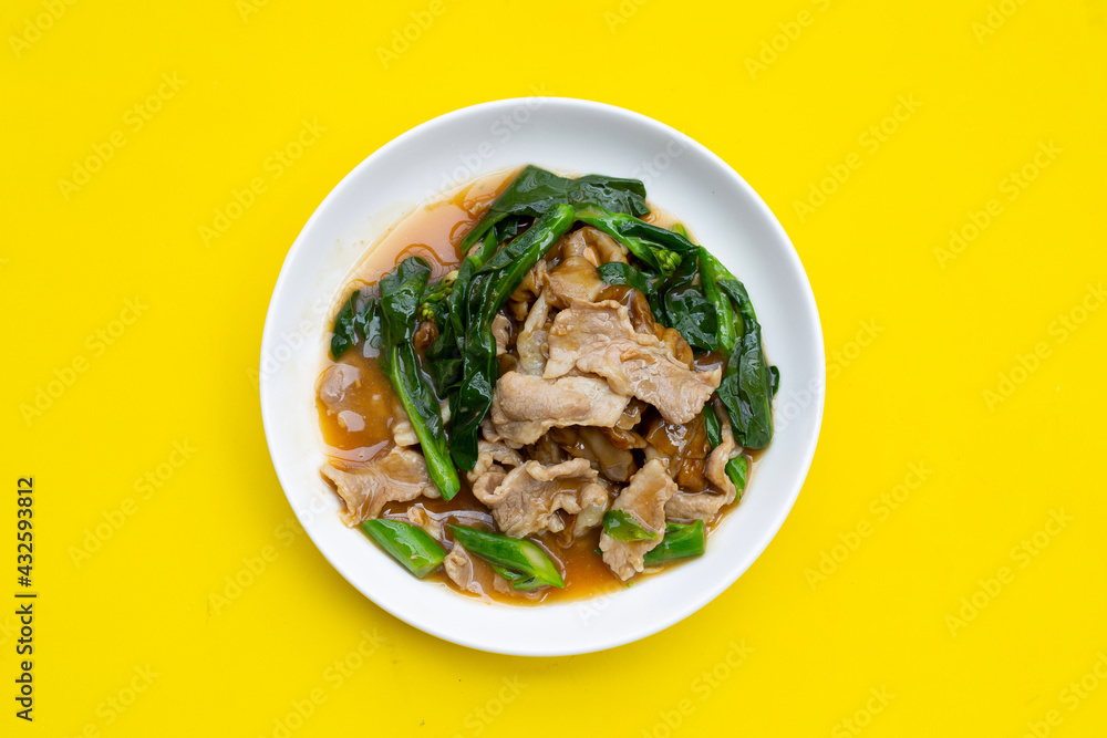 White plate of fried flat noodle with pork and kale in gravy sauce on yellow background.