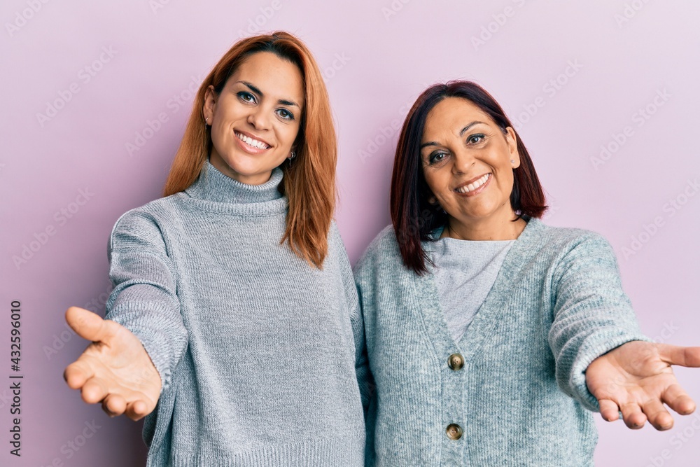 Latin mother and daughter wearing casual clothes smiling cheerful offering palm hand giving assistance and acceptance. Latin mother and daughter wearing casual clothes smiling cheerful offering palm hand giving assistance and acceptance.