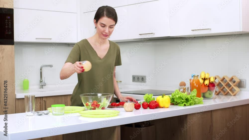 Attractive brunette woman is adding spices and salt in vegetable salad. Young wife is preparing dinner in the kitchen. Fresh vegetables are on the table Attractive brunette woman is adding spices and salt in vegetable salad. Young wife is preparing dinner in the kitchen. Fresh vegetables are on the table