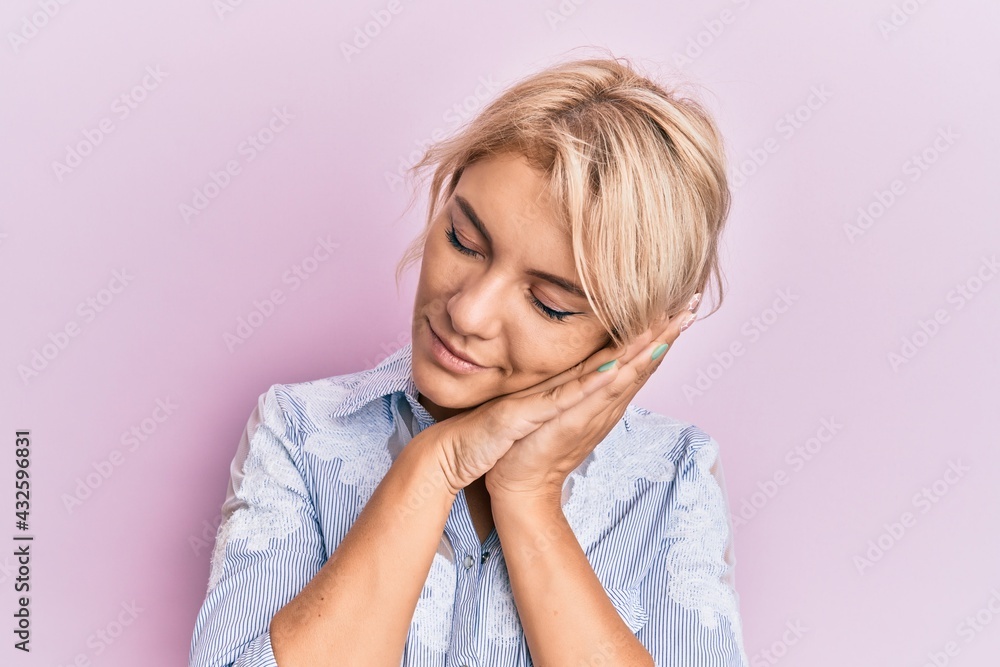 Young blonde girl wearing casual clothes sleeping tired dreaming and posing with hands together while smiling with closed eyes. Young blonde girl wearing casual clothes sleeping tired dreaming and posing with hands together while smiling with closed eyes.