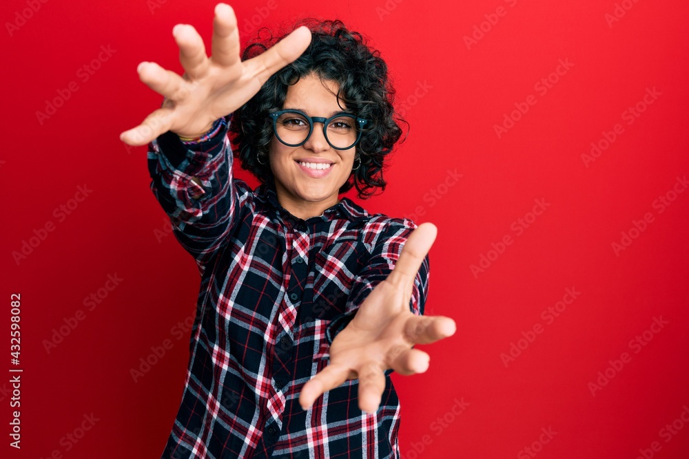 Young hispanic woman with curly hair wearing casual clothes and glasses looking at the camera smiling with open arms for hug. cheerful expression embracing happiness. Young hispanic woman with curly hair wearing casual clothes and glasses looking at the camera smiling with open arms for hug. cheerful expression embracing happiness.