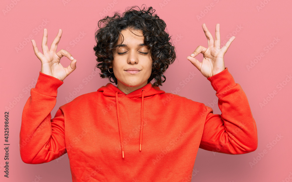 Young hispanic woman with curly hair wearing casual sweatshirt relax and smiling with eyes closed doing meditation gesture with fingers. yoga concept. Young hispanic woman with curly hair wearing casual sweatshirt relax and smiling with eyes closed doing meditation gesture with fingers. yoga concept.