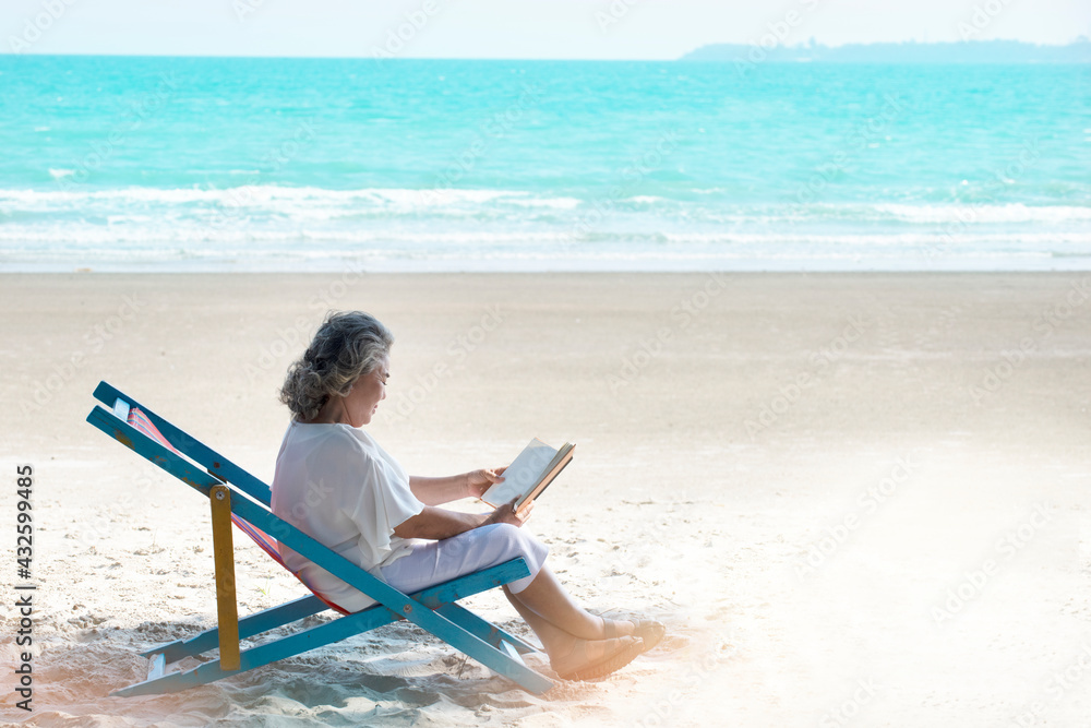 Portrait of a senior woman enjoying her free time by reading a book sitting near the beach. One relaxed people. 