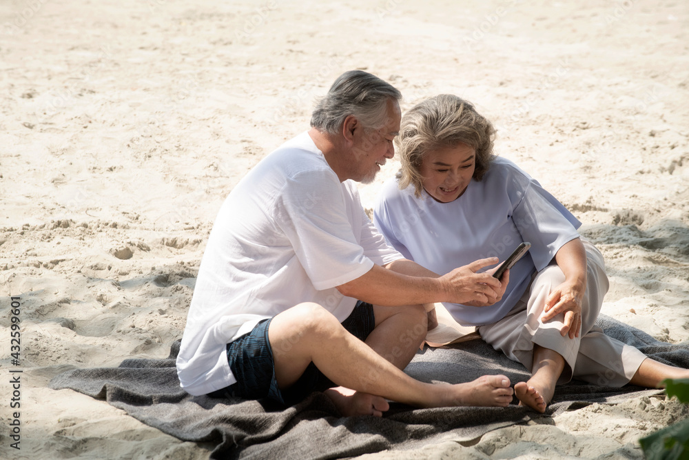 Two attractive senior people white-haired using smartphone camera sitting by the beach,Happy on the beach concept