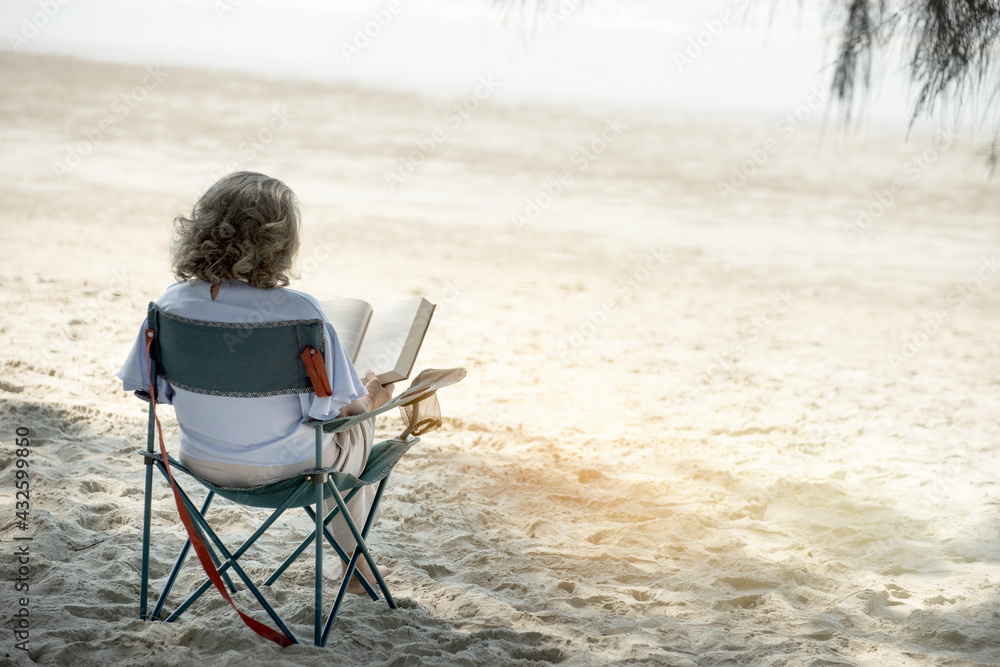 senior woman spending her free time sitting on beach relaxing during autumnal weather.