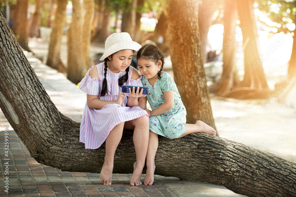 Obraz premium Cute two little kids girl using smartphone playing game in park