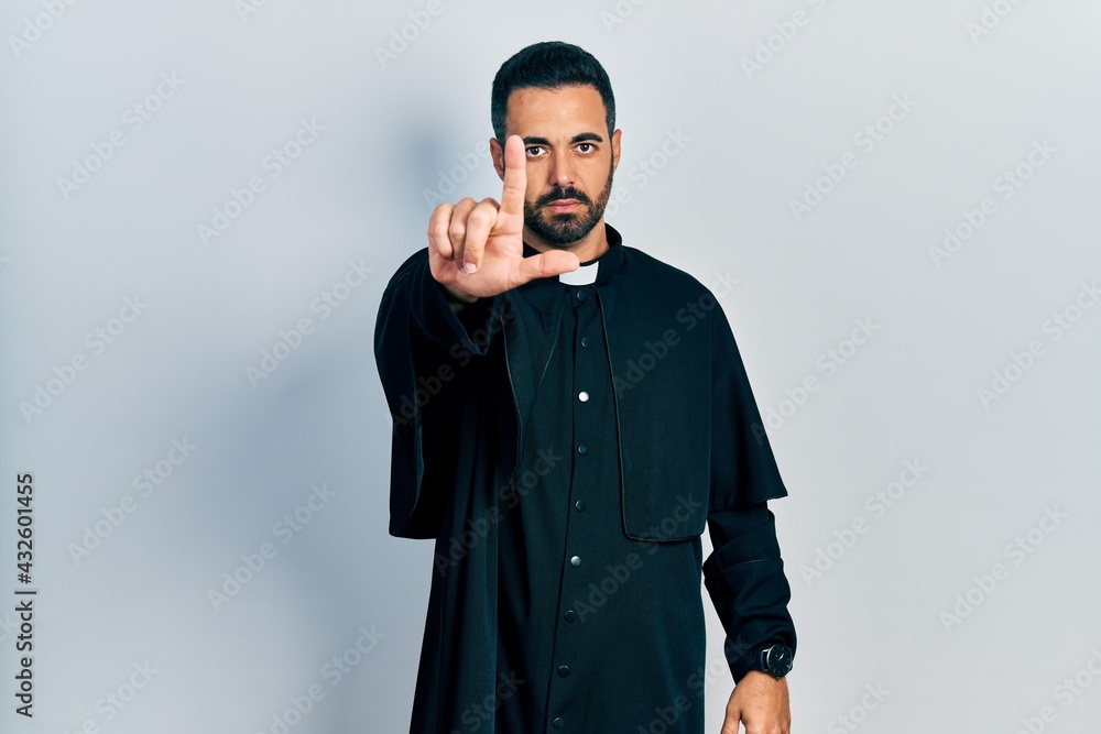 Handsome hispanic man with beard wearing catholic priest robe pointing with finger up and angry expression, showing no gesture Handsome hispanic man with beard wearing catholic priest robe pointing with finger up and angry expression, showing no gesture