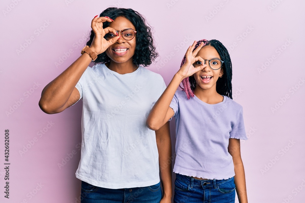 Beautiful african american mother and daughter wearing casual clothes and glasses doing ok gesture with hand smiling, eye looking through fingers with happy face. Beautiful african american mother and daughter wearing casual clothes and glasses doing ok gesture with hand smiling, eye looking through fingers with happy face.