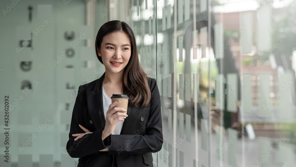 Beautiful Asian businesswoman stand leaning at the large mirror and holding coffee at the office. Beautiful Asian businesswoman stand leaning at the large mirror and holding coffee at the office.