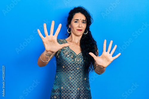 Young woman wearing bindi and traditional kurta dress afraid and terrified with fear expression stop gesture with hands, shouting in shock. panic concept.