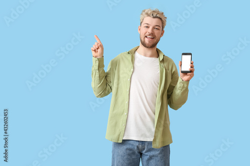Young man with mobile phone pointing at something on color background
