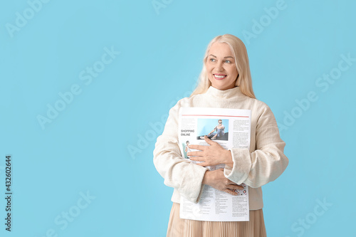 Mature woman with newspaper on color background