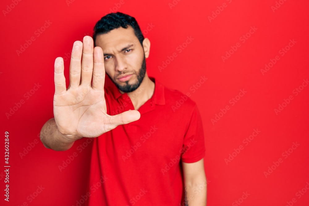 Hispanic man with beard wearing casual red t shirt doing stop sing with palm of the hand. warning expression with negative and serious gesture on the face. Hispanic man with beard wearing casual red t shirt doing stop sing with palm of the hand. warning expression with negative and serious gesture on the face.
