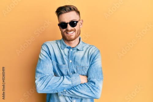 Young redhead man wearing stylish sunglasses happy face smiling with crossed arms looking at the camera. positive person.