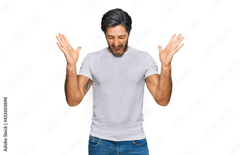 Young hispanic man wearing casual white t shirt celebrating mad and crazy for success with arms raised and closed eyes screaming excited. winner concept Young hispanic man wearing casual white t shirt celebrating mad and crazy for success with arms raised and closed eyes screaming excited. winner concept