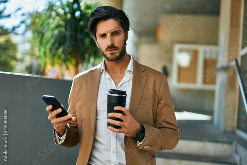 Young hispanic businessman using smartphone and drinking coffee at the city.